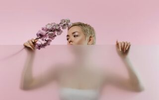 A short-haired woman holding flowers looks over a frosted glass panel.