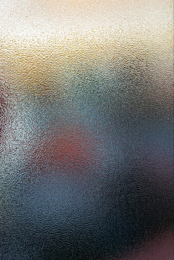 A pane of obscured glass with blurred color and light showing through the glass.