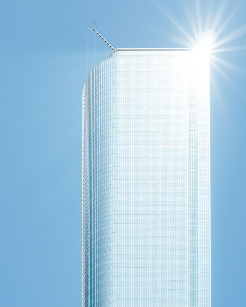 A brilliant sun reflects blindingly off a glass-covered high-rise building.