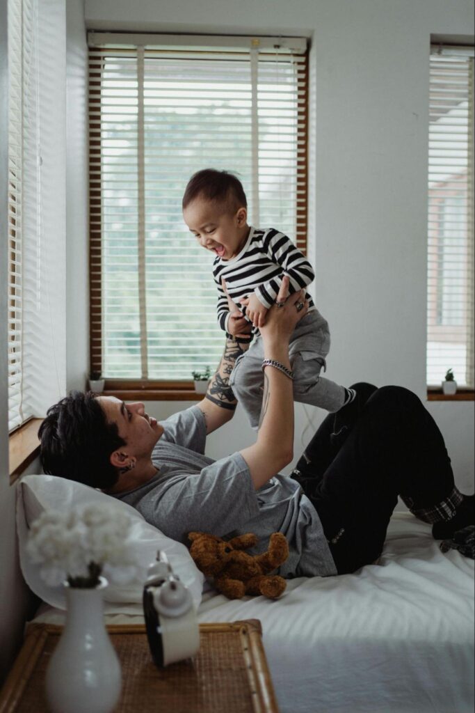 Man with Baby on a Bed Next to Windows with Blinds